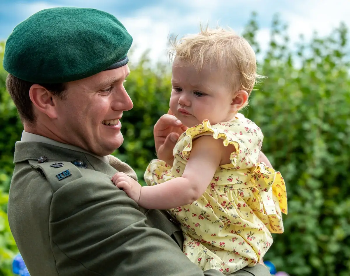 Father in military uniform holding young daughter outdoors